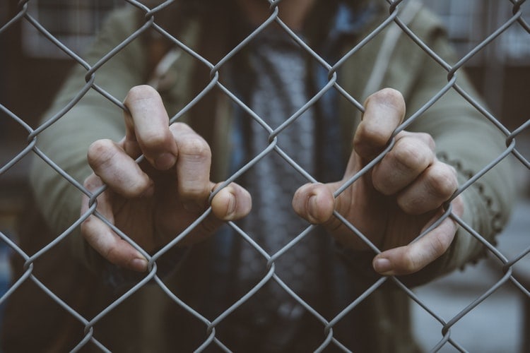 Person's hands grabbing hold of a metal fence