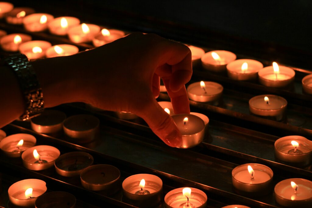 person setting white votive candle beside other candles in a church